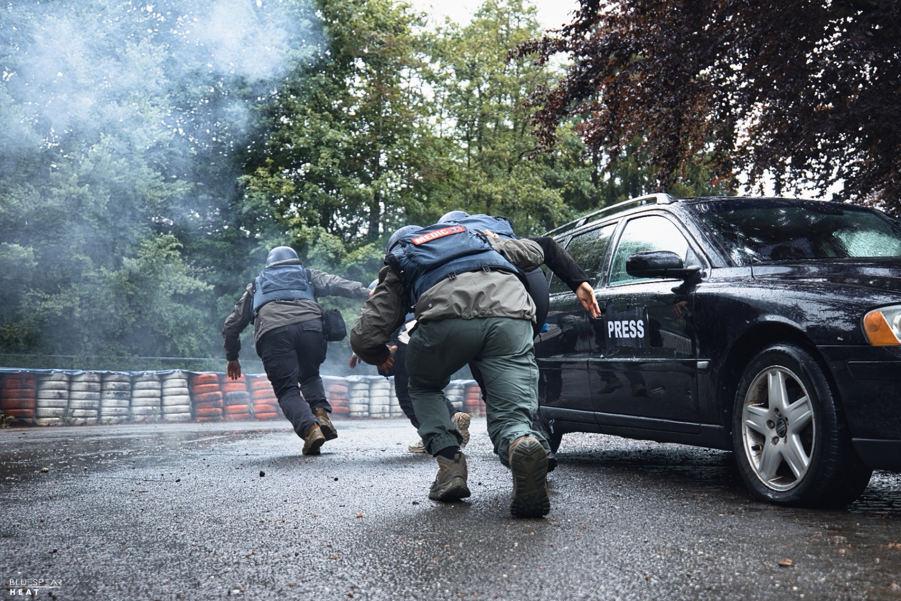 Medic moving casualty behind press car under smoke