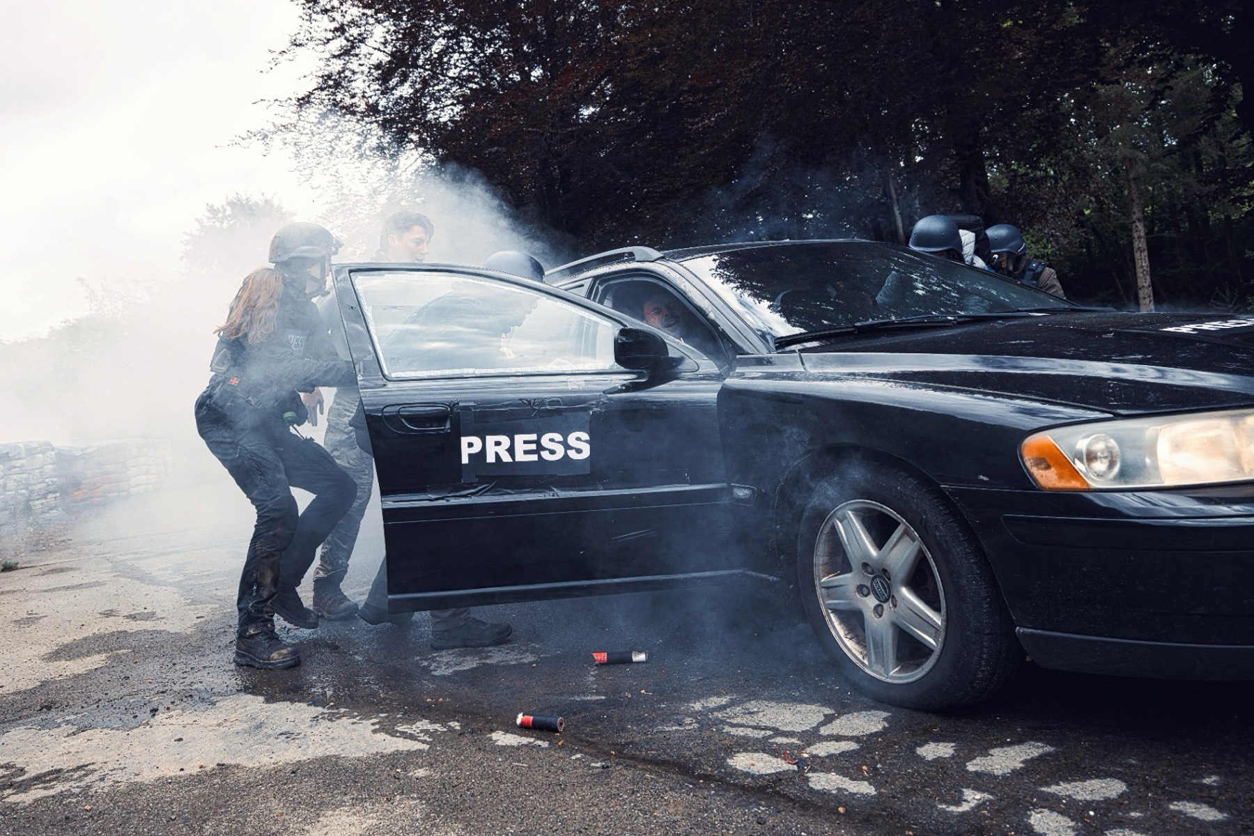 Hostile Environment Awareness Training – journalists taking cover behind a PRESS vehicle under smoke